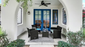 Une terrasse couverte, meublée de meubles en osier, avec un ventilateur de plafond et une porte bleue.