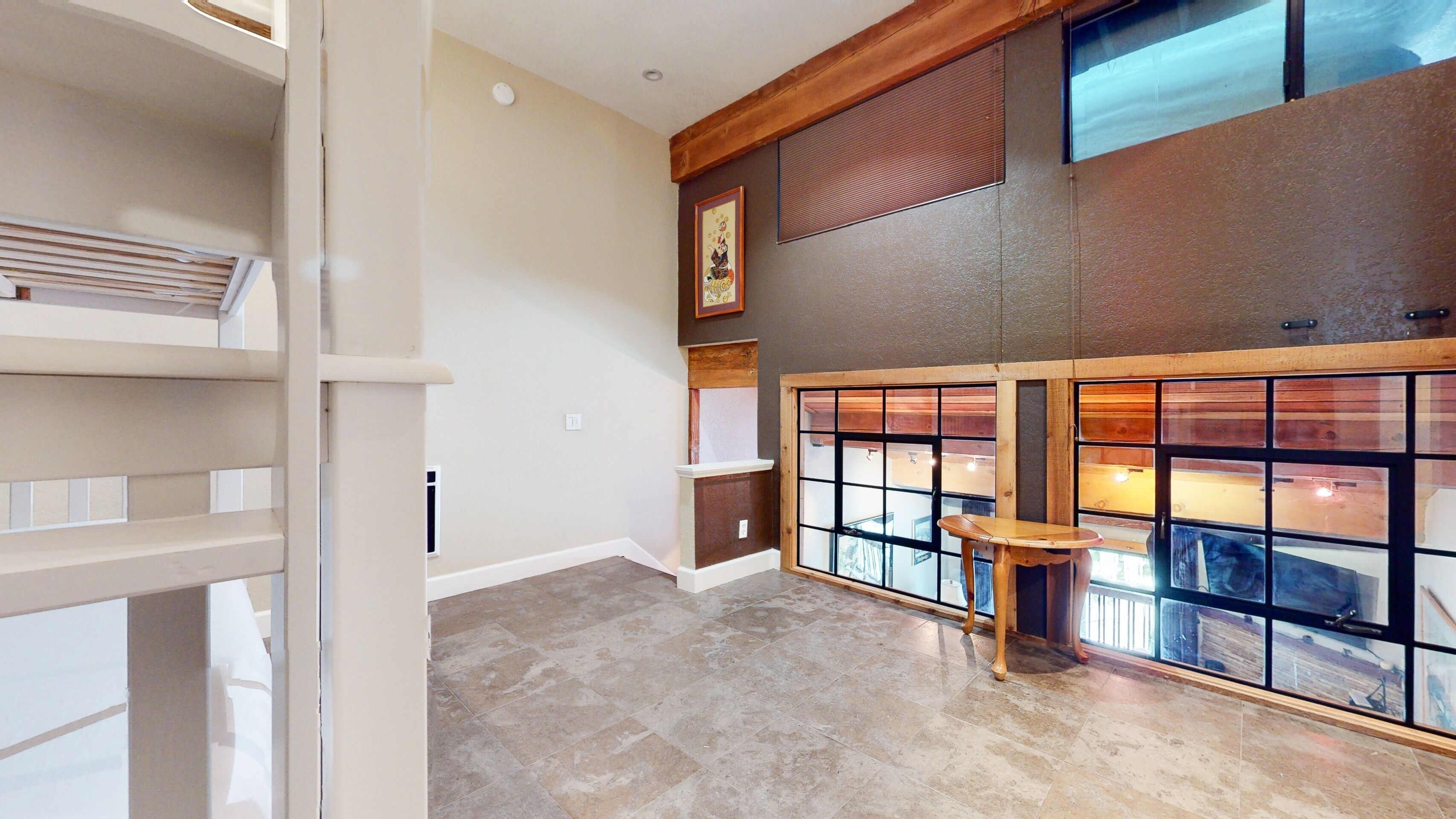 A spacious room with a high ceiling, large windows with wooden frames, a built-in bench, and a fireplace.