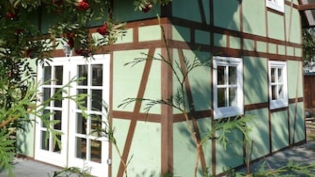Una casa tradizionale con struttura a graticcio, tetto in tegole rosse, finestre con cornice bianca e facciata verde.