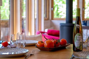 Une table à manger avec une bouteille de vin, des verres, des assiettes et un saladier de tomates.