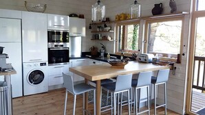 Cocina compacta con una mesa de madera, cuatro sillas, lavadora y ventana con vista a árboles.