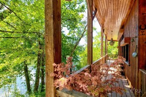 Une cabane en bois dotée d’un porche donnant sur une zone boisée et un plan d’eau.