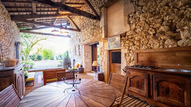Une cuisine rustique avec des murs en pierre, une table ronde en bois, des armoires en bois et un mur en pierre.