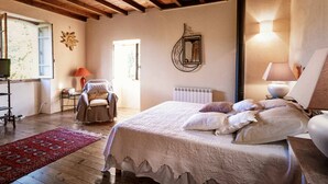 Une chambre confortable avec un plafond en bois, un lit recouvert de plusieurs coussins, une chaise, un tapis rouge et un miroir fixé au mur.