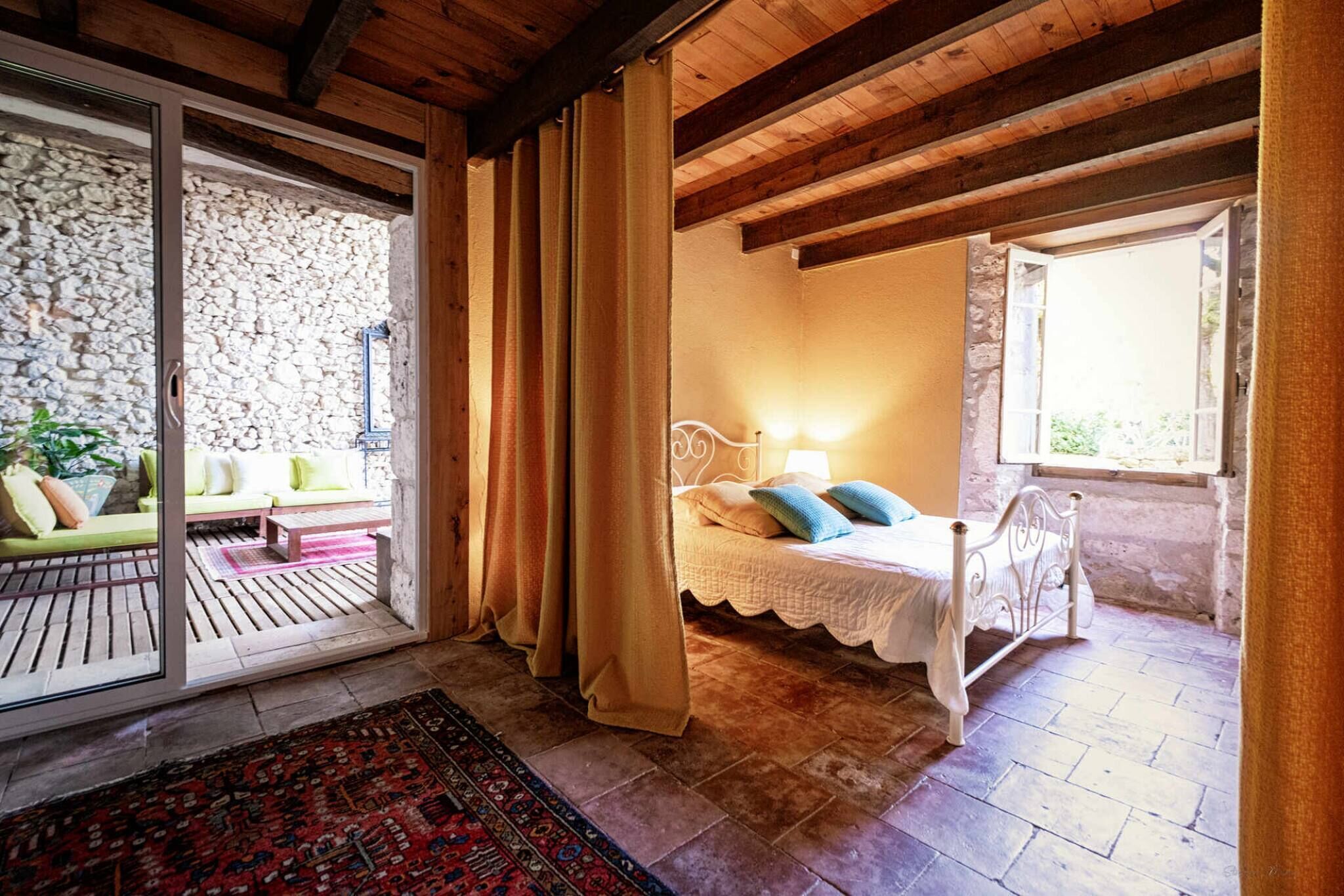 Een slaapkamer met een stenen muur, een bed met witte beddengoed en een raam met gordijnen.