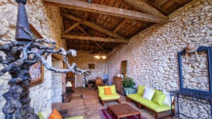 Une pièce rustique aux murs de pierre, avec des poutres en bois, une cheminée en pierre, une table en bois et un canapé agrémenté de coussins.
