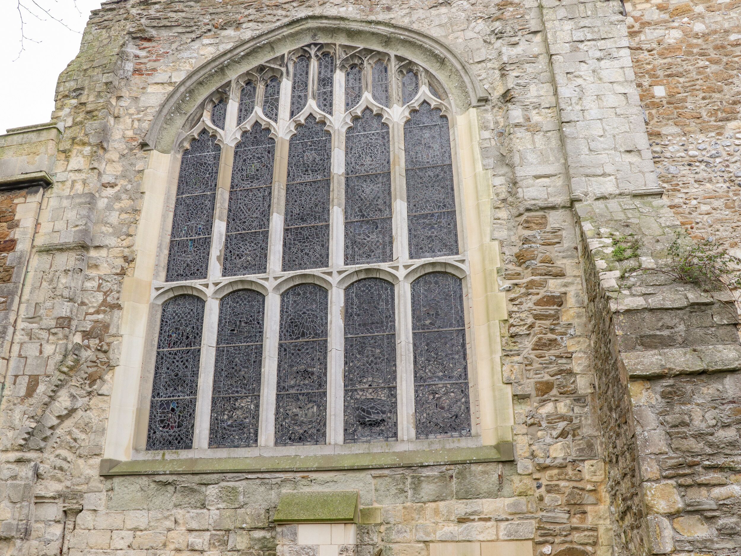 A stone building with a large arched window featuring intricate tracery and stained glass.