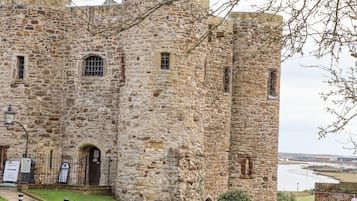 A stone castle with a grassy courtyard, a black gate, and a river in the background.