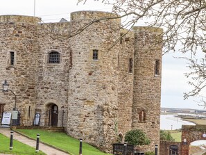 A stone castle with a grassy courtyard, a black gate, and a river in the background.