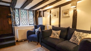A cozy living room with a dark blue sofa, patterned cushions, a small armchair, and a vintage-style rug. - Church View (Rye)
