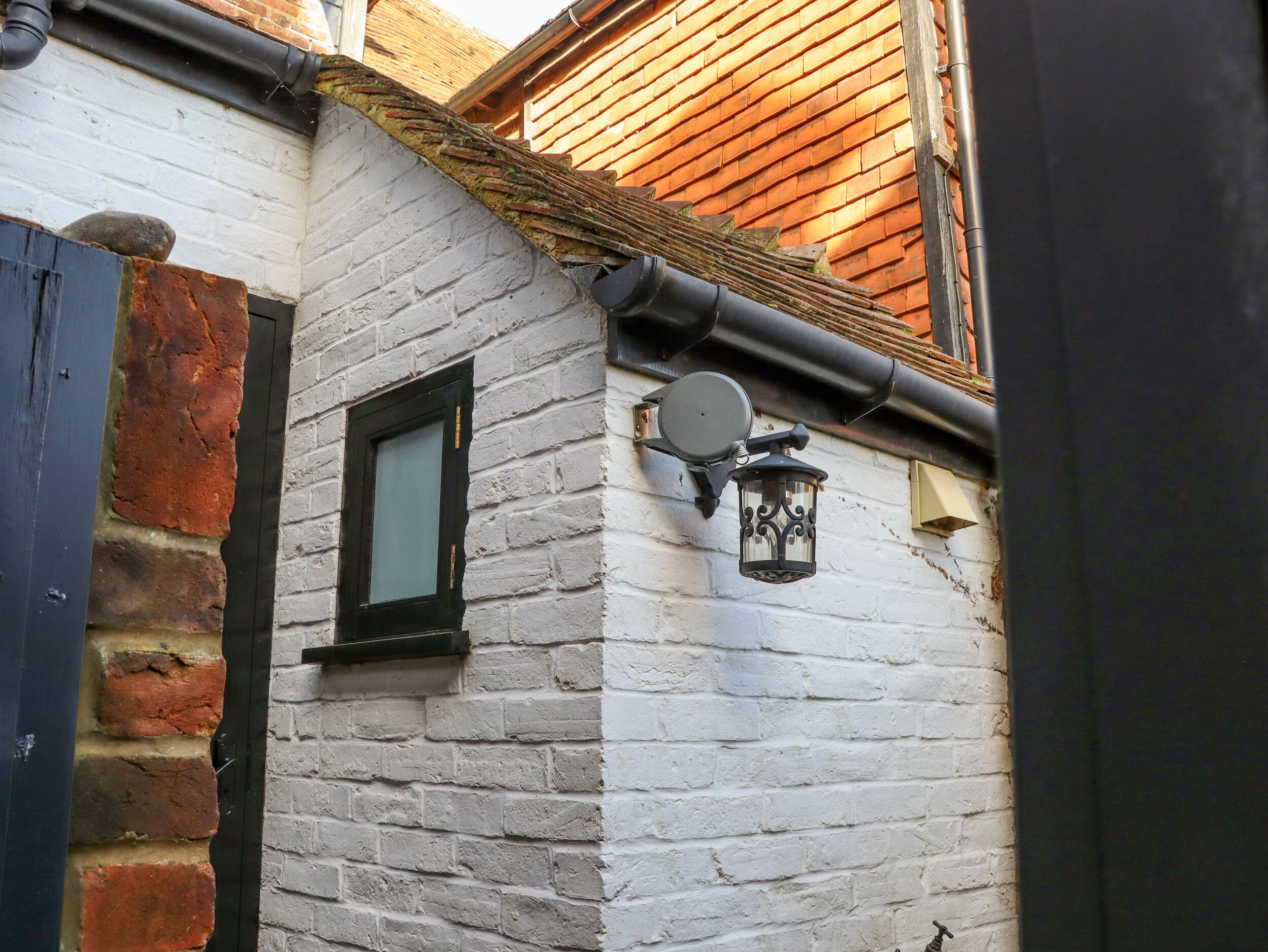 Un bâtiment en briques blanches avec une porte noire, une petite fenêtre et une lanterne fixée au mur.