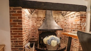 A brick fireplace with a modern vent hood, a table with a glass of wine, and a basket of flowers. - Church View (Rye)