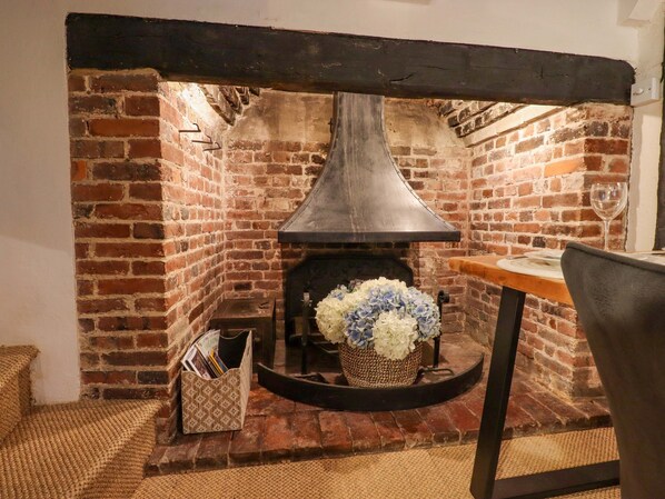 Une cheminée en briques avec une hotte de ventilation moderne, une table avec une bouteille de vin et un panier de fleurs.