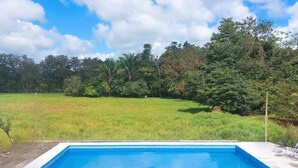 A rectangular swimming pool with a concrete edge, surrounded by a grassy field and trees. - Breeze #4 - Brisas Griegas Vacations (Quepos)