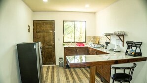 A compact kitchen with a refrigerator, wooden cabinets, a countertop, and a window. - Breeze #4 - Brisas Griegas Vacations (Quepos)