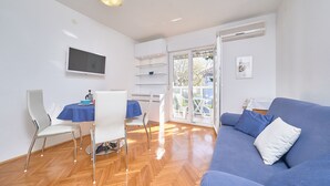 Una sala de estar moderna con un sofá azul, una mesa de comedor con sillas y un televisor montado en la pared.