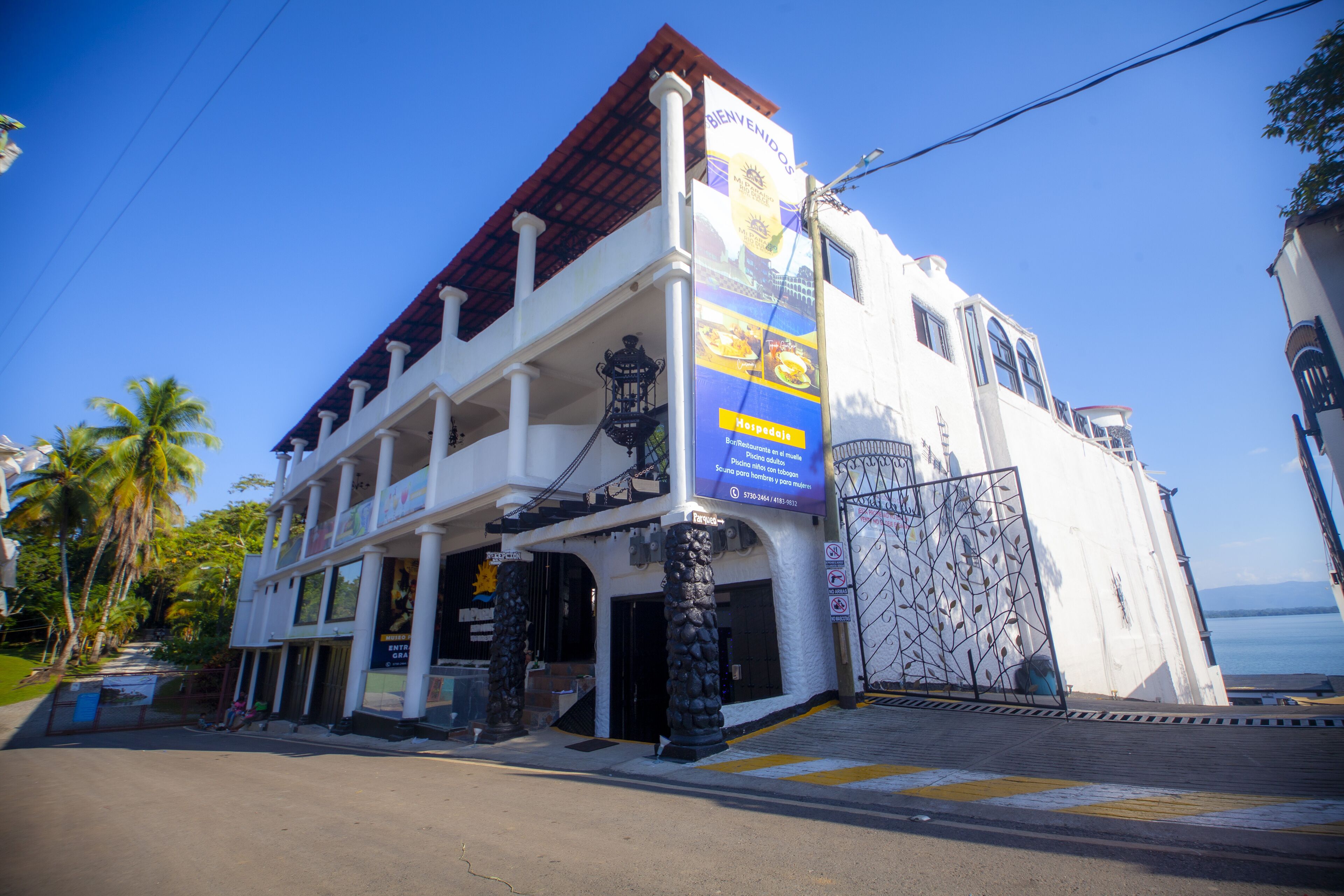 A white building with a red roof and multiple balconies. There is a large sign on the building and a gate with a decorative metal design.