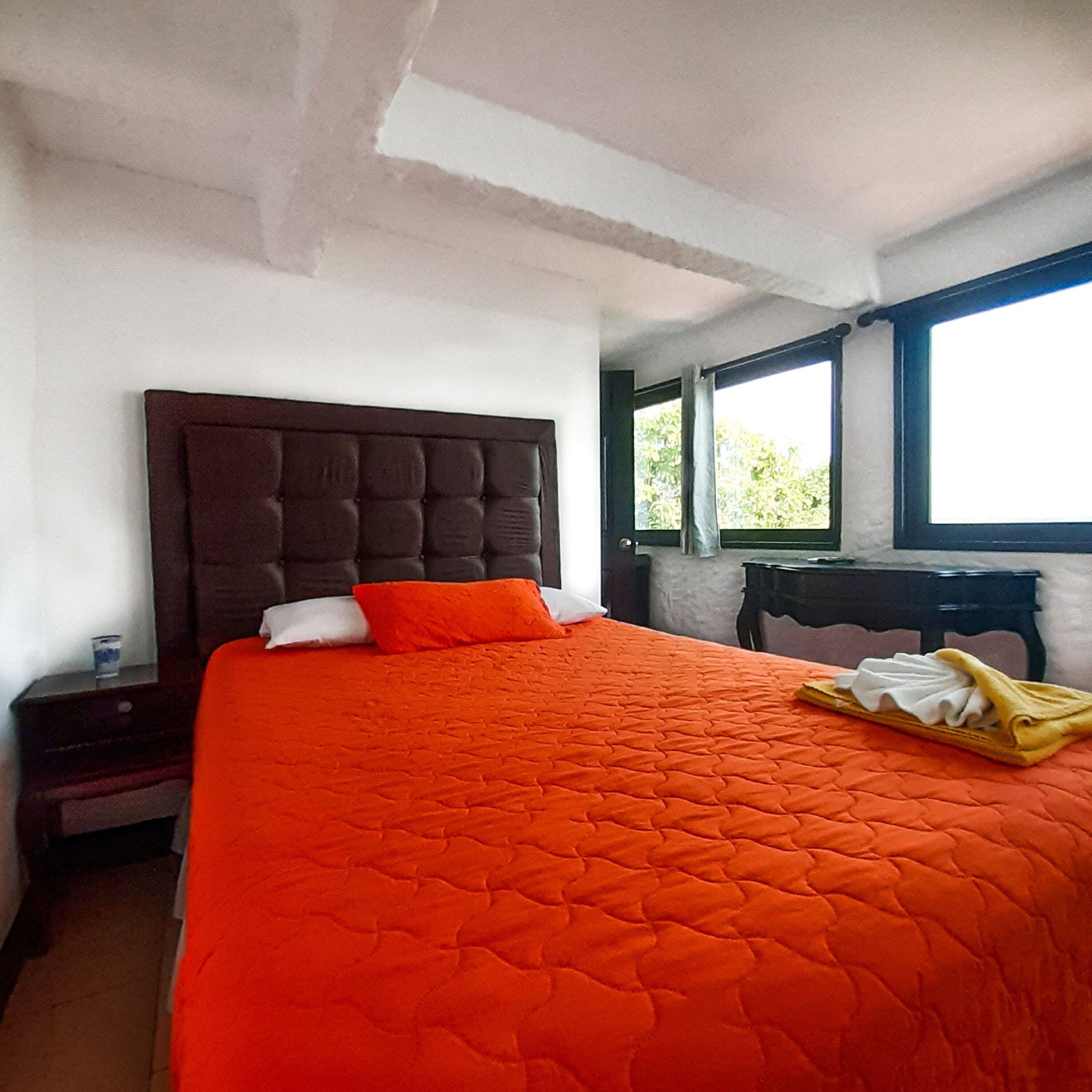 A bedroom with a large bed, a nightstand, a window, and a view of greenery outside.