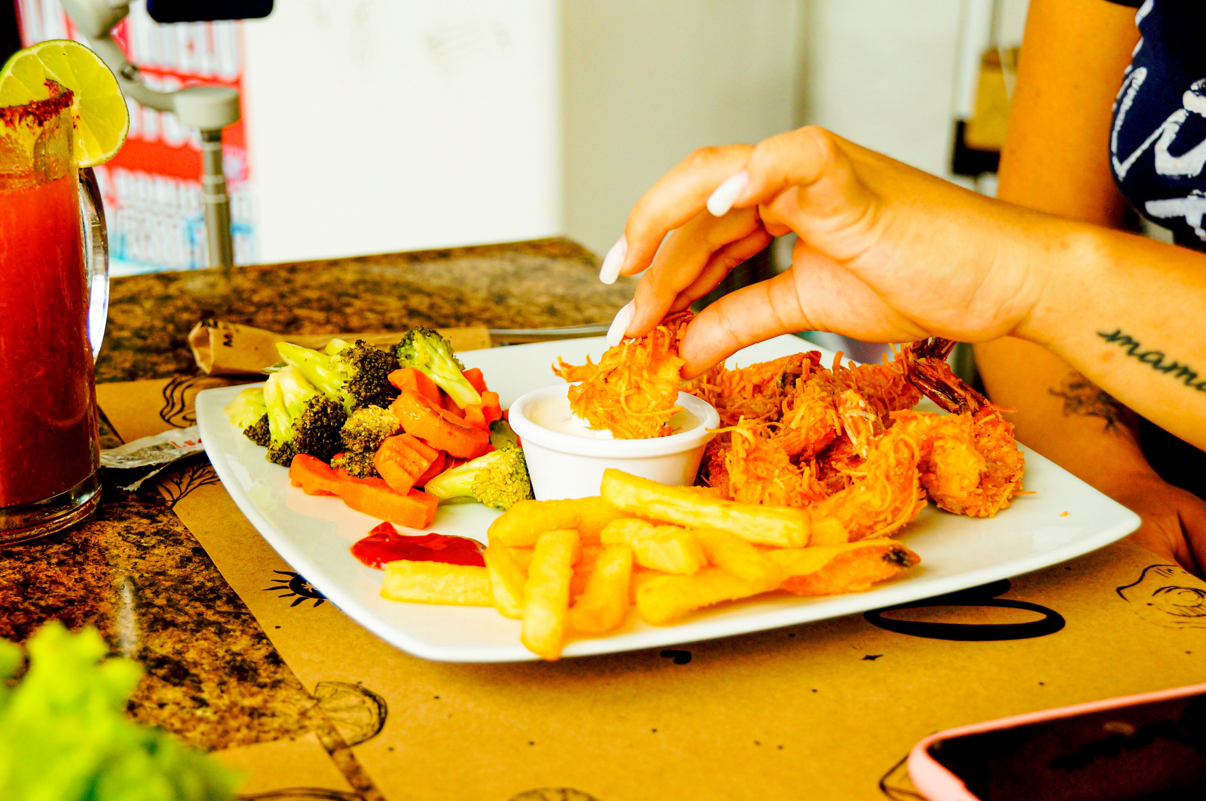A plate of food including shrimp, fries, and vegetables, with a drink in the background.