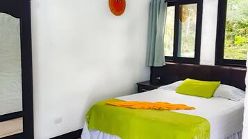 Un dormitorio con cama, mesita de noche, ventana con cortinas y termostato instalado en la pared.
