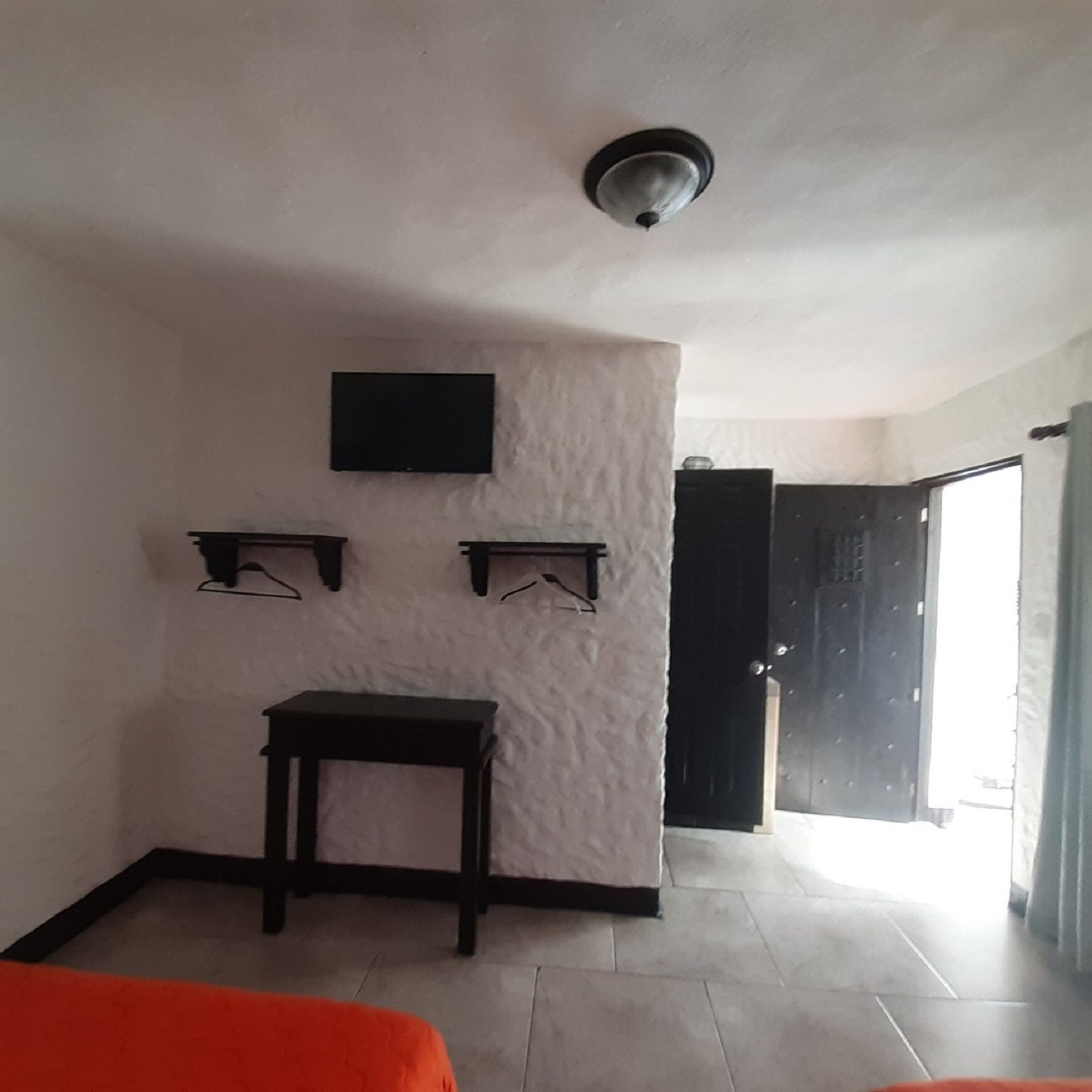 A room with a white textured wall, a flat-screen TV mounted above a small table, and two wall-mounted shelves.