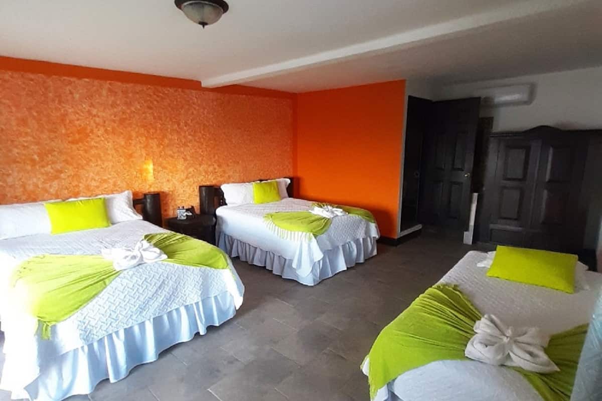 Et hotelværelse med tre senge, hver med et hvidt og grønt sengetæppe, og en væg med orange struktur.