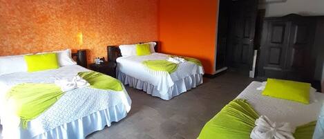 A hotel room with three beds, each with a white and green bedspread, and an orange textured wall.