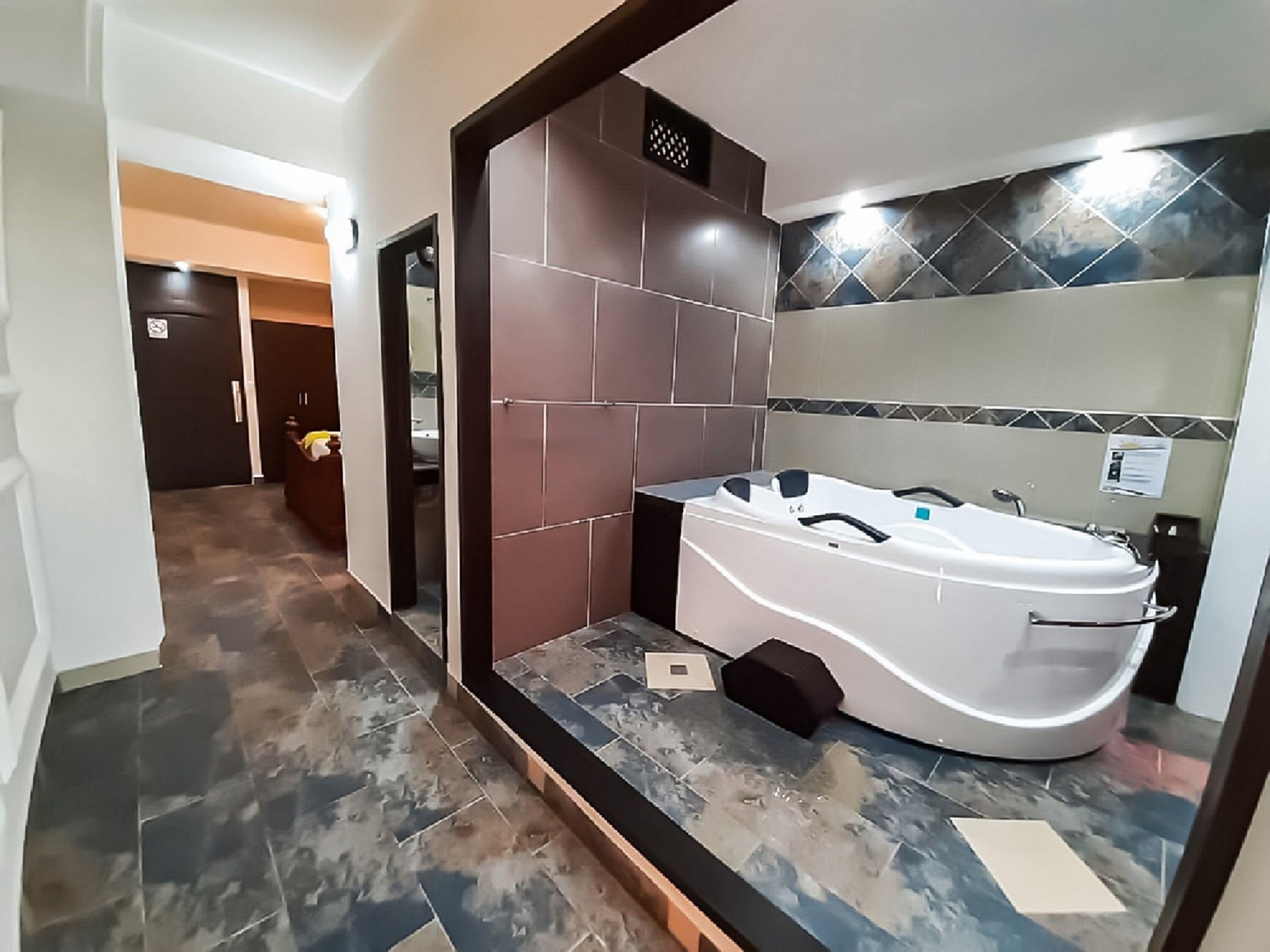 Un baño moderno con una bañera independiente, azulejos oscuros con diseño y una zona de ducha revestida.
