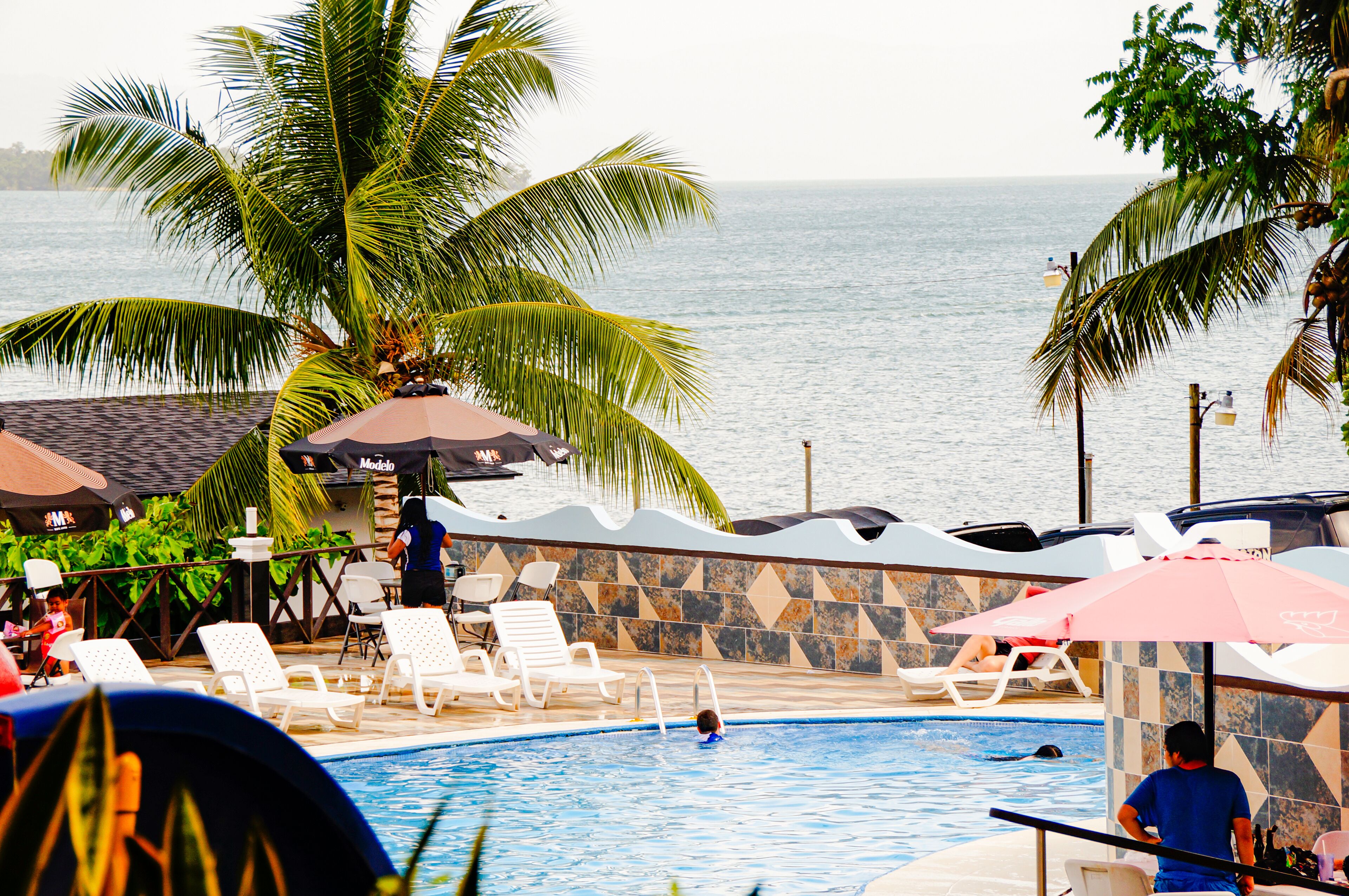 A pool area with lounge chairs, umbrellas, and a view of the sea.