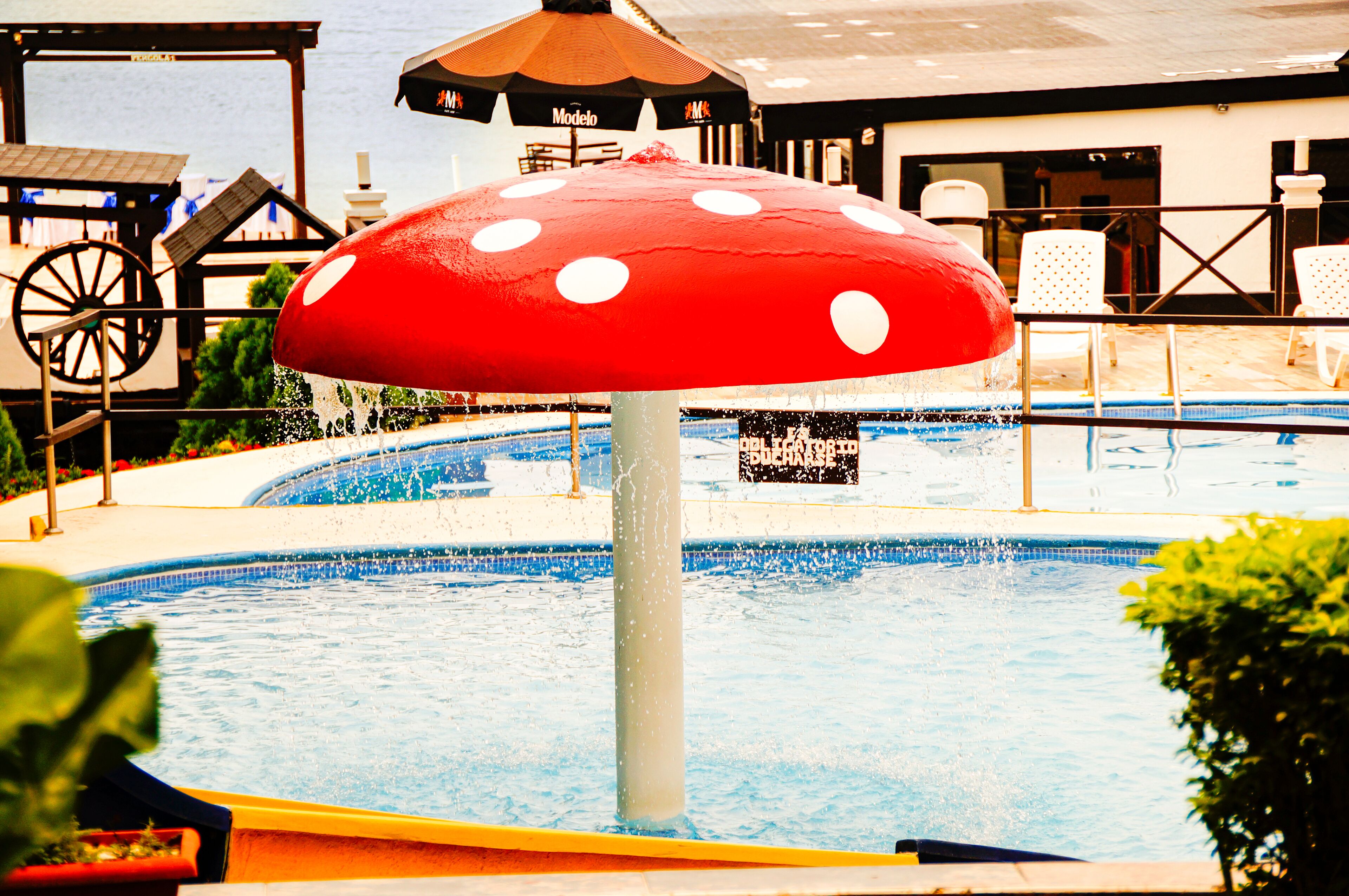 Een zwembad met een grote, paddenstoelvormige parasol, een waterrad en een bord waarop 'Bucharest' staat.