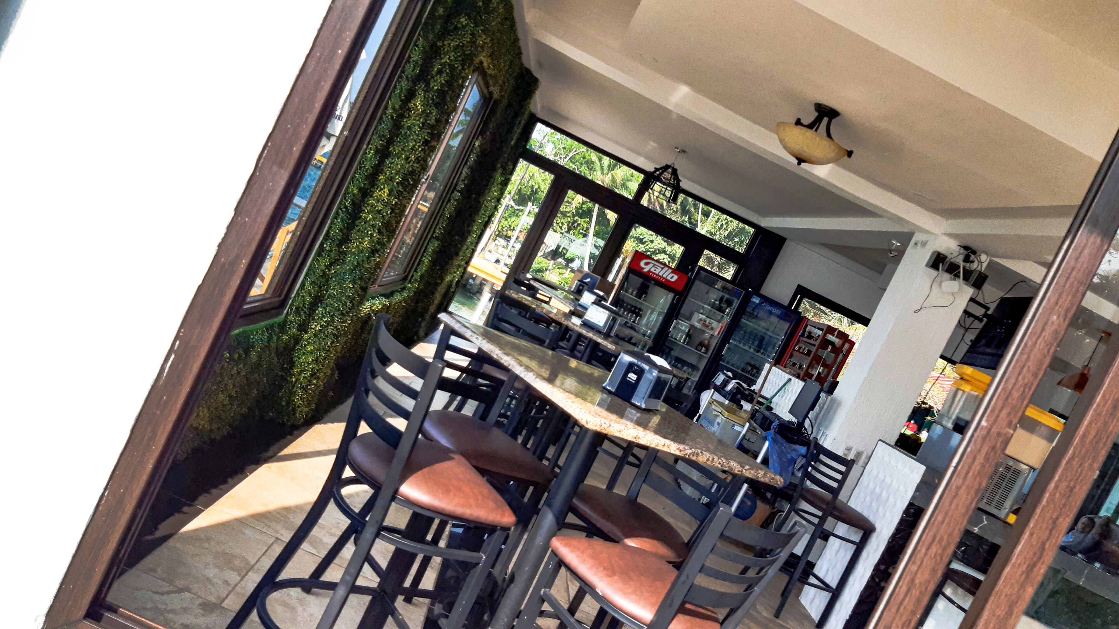 Un espace de détente intérieur doté d’un haut plafond, un coin bar avec un comptoir et des tabourets, et une vue sur l’extérieur grâce à de grandes fenêtres.