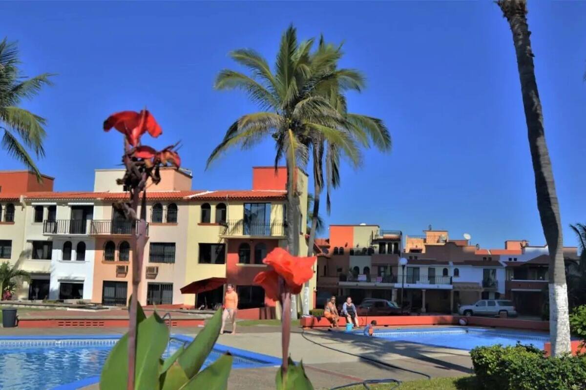 Ein Hotel mit Swimmingpool, Palmen und einer roten Blume im Vordergrund.