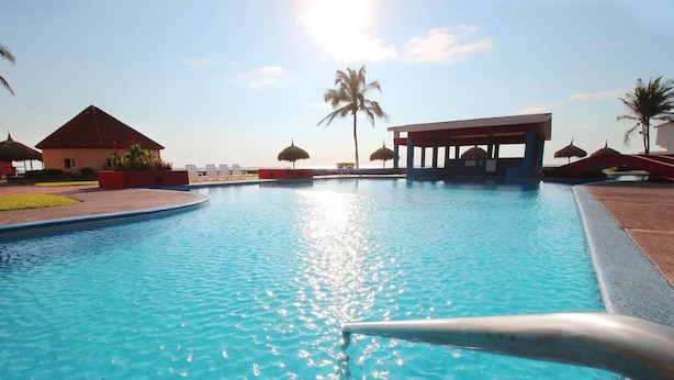 A swimming pool with a clear blue water surface, surrounded by lounge chairs and palm trees. - Casas RDM (Mazatlán)