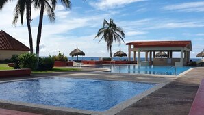 A pool area with a clear view of the ocean, palm trees, and a thatched-roof structure. - Casas RDM (Mazatlán)