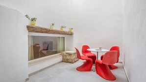 A small, modern room with a glass wall, a stone ledge with plants, and a table with red chairs.