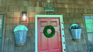 Entrada de una cabaña con puerta roja, un adorno de corona verde, decoración de astas y dos cestas metálicas a cada lado.
