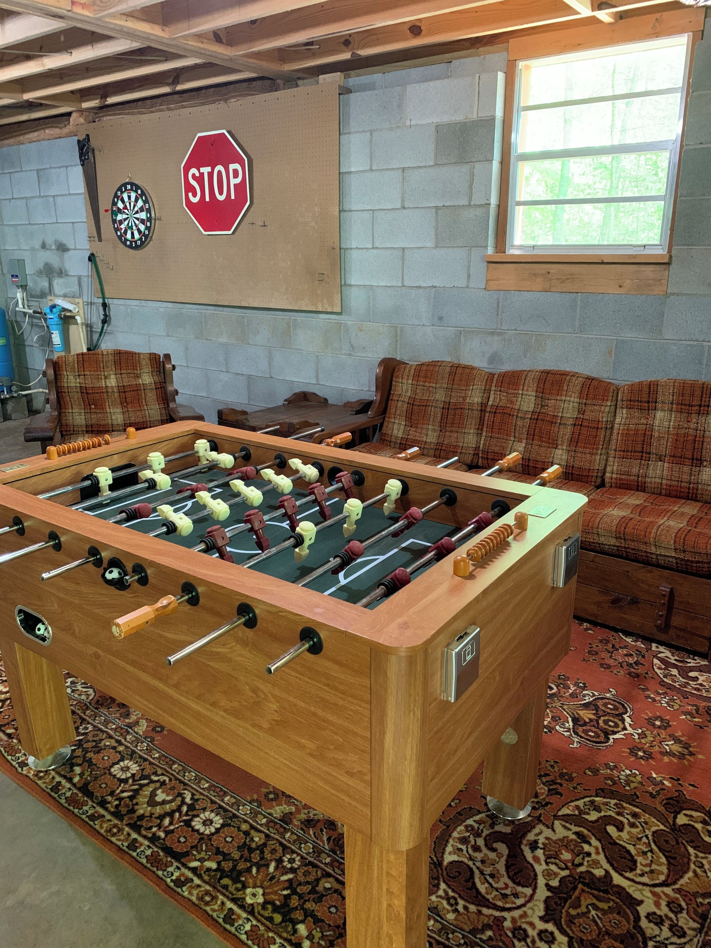 A foosball table in a room with a plaid sofa, a stop sign, and a dartboard.