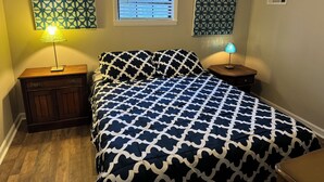 Un dormitorio con una cama, dos mesitas de noche, un ventanal con persianas y decoración mural con estampado.