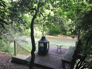 Une terrasse en bois avec une lanterne, un banc et une vue sur une rivière.