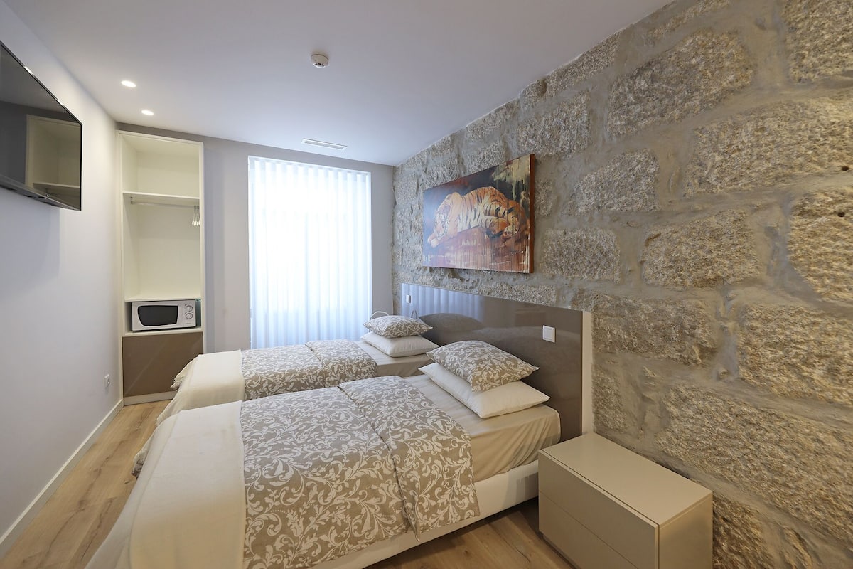 A bedroom with two beds, a stone wall, a mounted painting, a TV, and a microwave.
