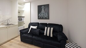 A modern living space with a black sofa, white and black striped pillows, a marble-tiled kitchen area, and a chandelier artwork on the wall. - FLH Porto Downtown GuestHouse (Porto)