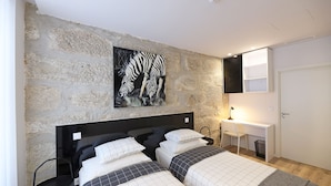 A bedroom with two beds, a stone wall, a zebra painting, a desk, and a chair. - FLH Porto Downtown GuestHouse (Porto)