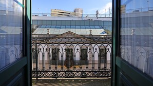 A view through a window with a wrought iron fence, a building with a glass roof, and a clear blue sky. - FLH Porto Downtown GuestHouse (Porto)