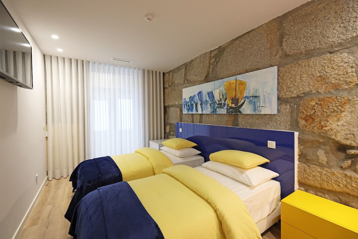 A hotel room with two beds, a stone wall, a painting, and a TV.