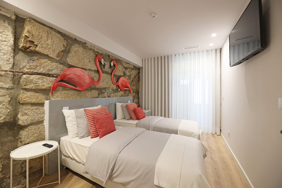 A hotel room with two beds, a stone wall, a flat-screen TV, and a small table.