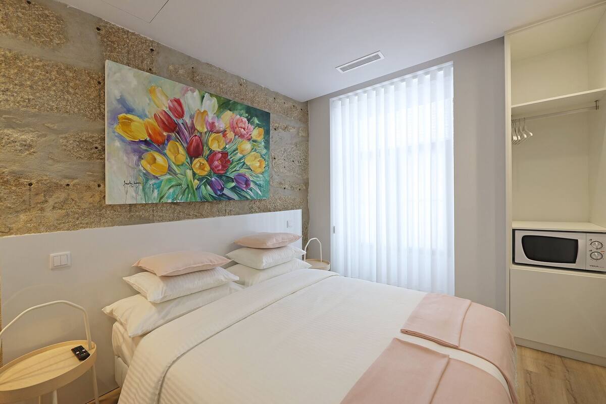 A bedroom with a bed, a painting of flowers, a shower, and a microwave.