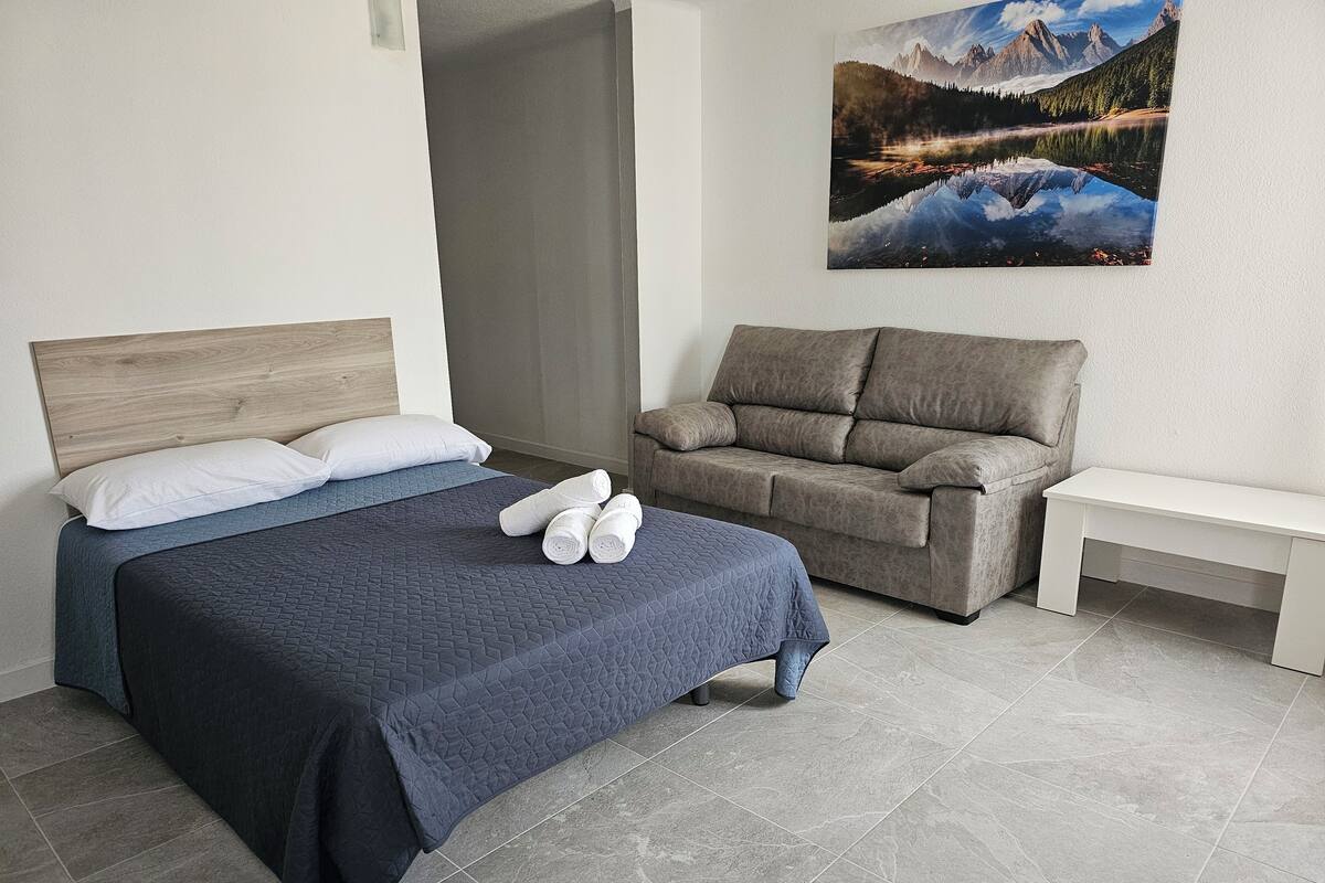 A bedroom with a bed, a sofa, a bench, and a painting of a mountain landscape.