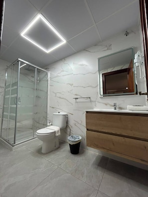 Un baño moderno con cabina de ducha de vidrio, inodoro, tocador con espejo y un cubo de basura.