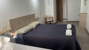 A hotel room with two beds, a chair, a bedside table, and a wardrobe.