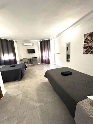 Habitación de hotel con dos camas, un escritorio, una silla, un televisor y una ventana con cortinas.